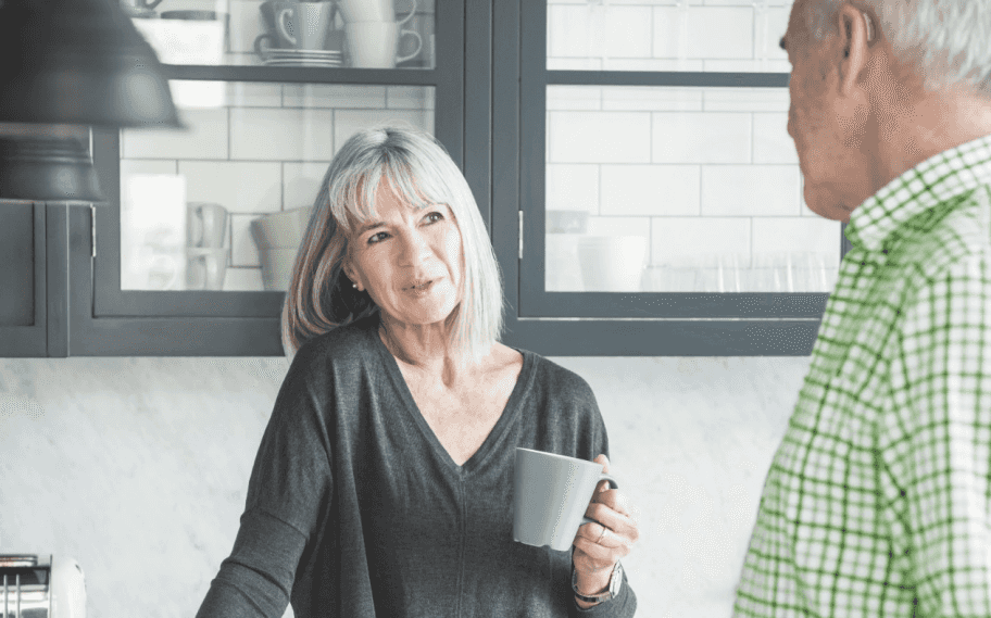 man talking to wife holding coffee cup hearing aid